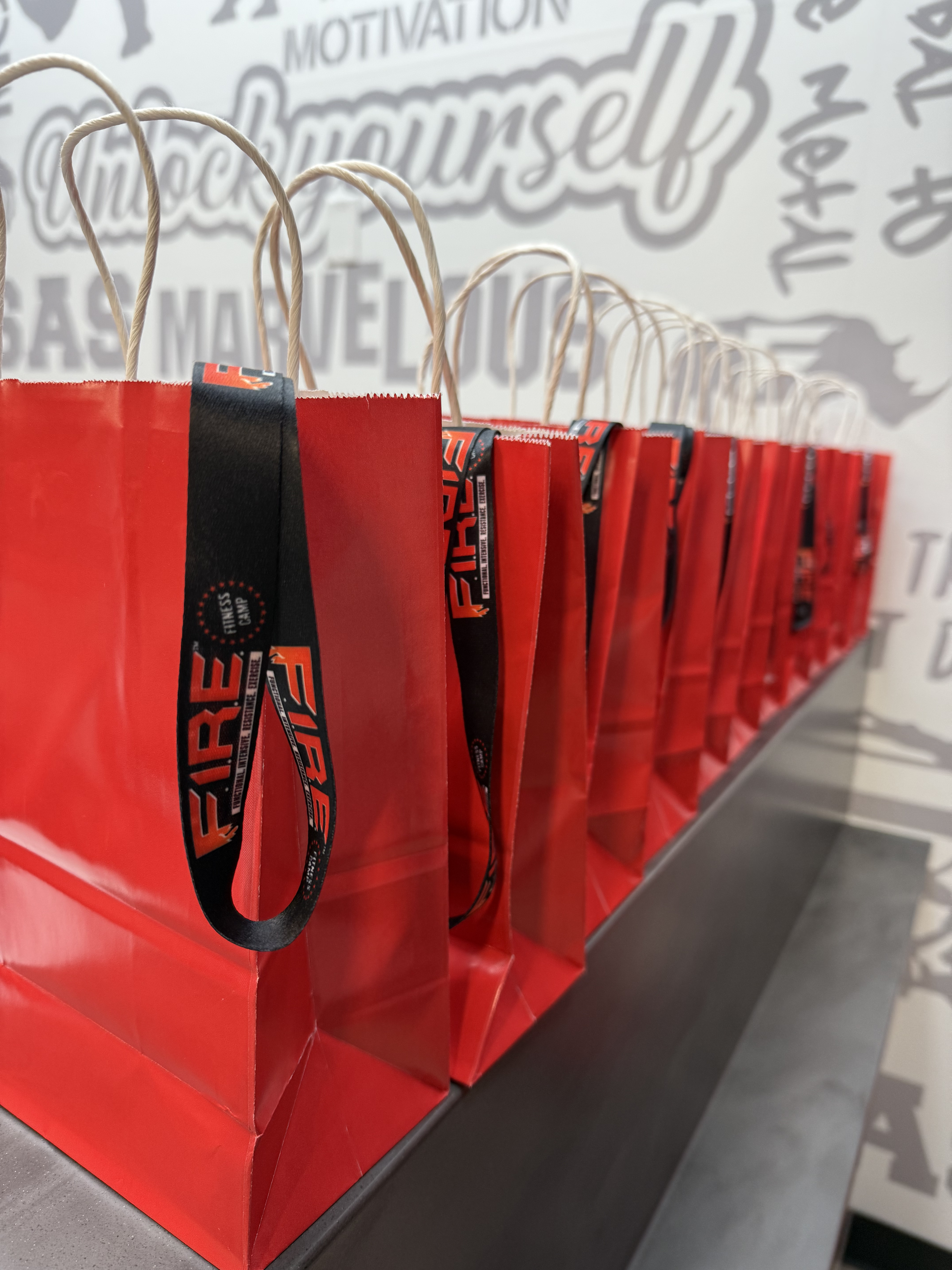 Row of red FIRE-branded gift bags lined up along the motivation wall