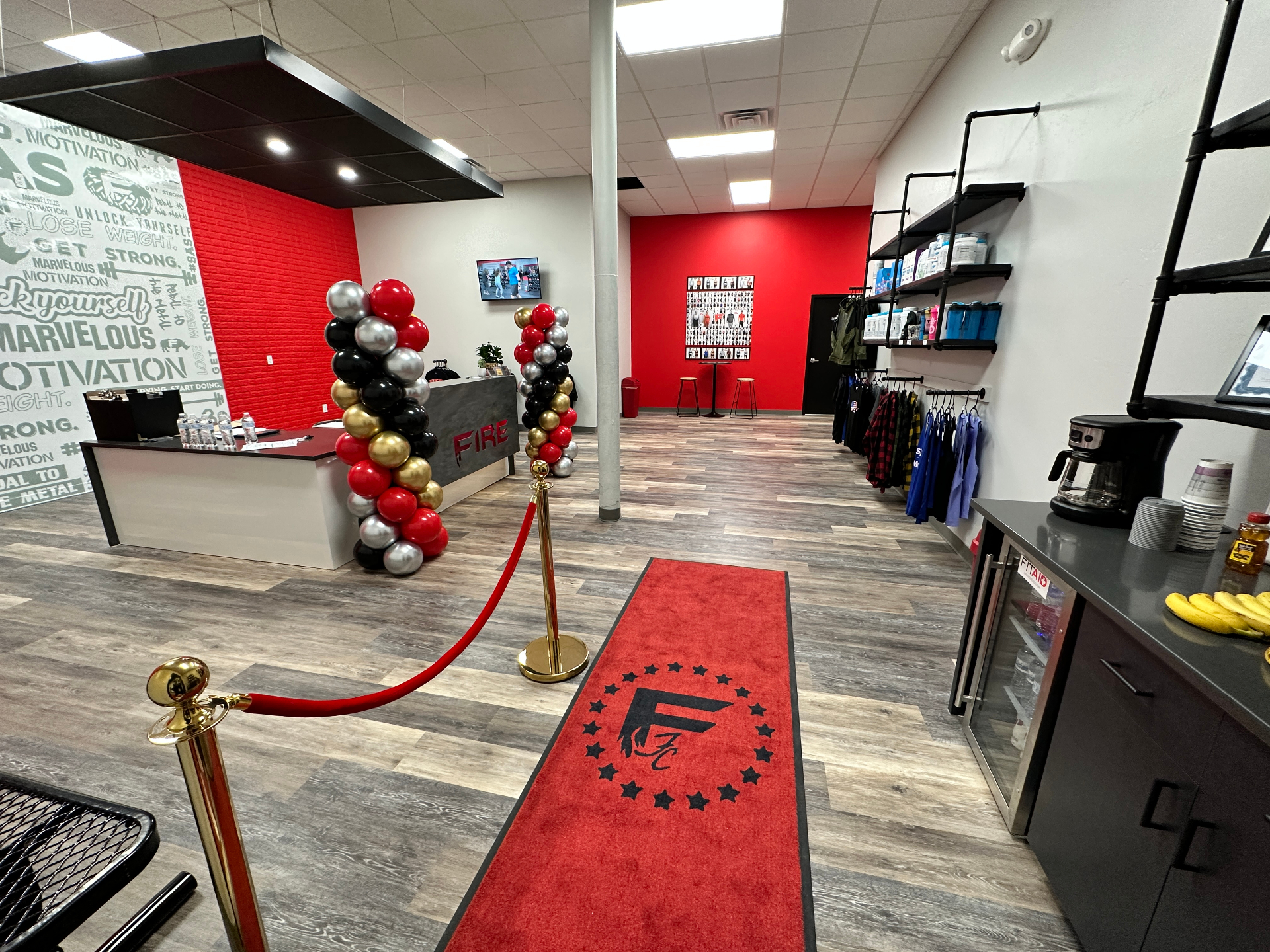FIRE Fitness Camp lobby entrance with branded red carpet, front desk, and retail wall